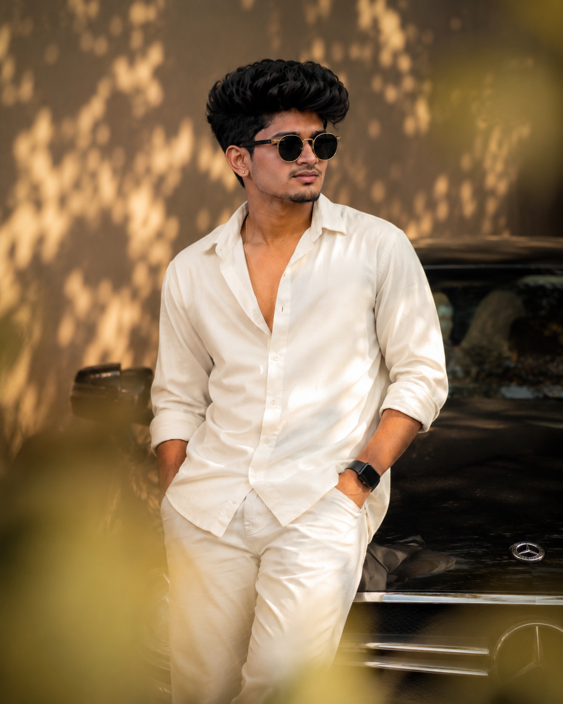 Ultra-realistic cinematic portrait of a confident young Indian man wearing a cream-white shirt, gold chain, and round sunglasses with warm golden sunlight, dramatic shadows, and DSLR-quality detail.